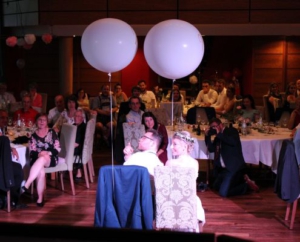 Brautpaar bei einer Hochzeit sitzt auf Stühlen mit 2 großen Luftballons zum Thema Wann ist der beste Zeitpunkt, um einen DJ für die Hochzeit zu buchen?